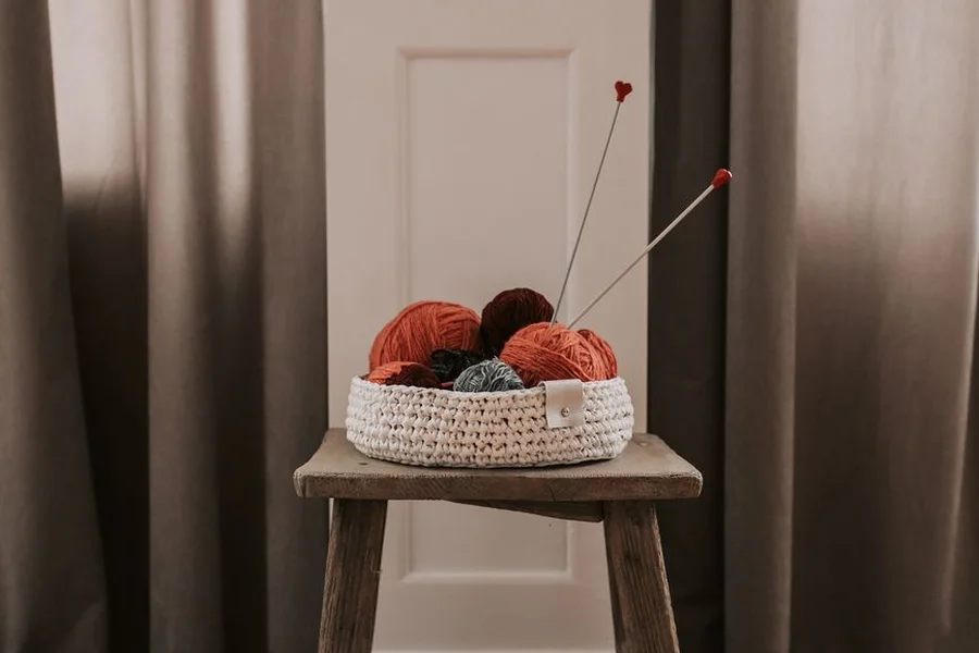 A wooden yarn bowl holding a ball of soft yarn on a rustic table