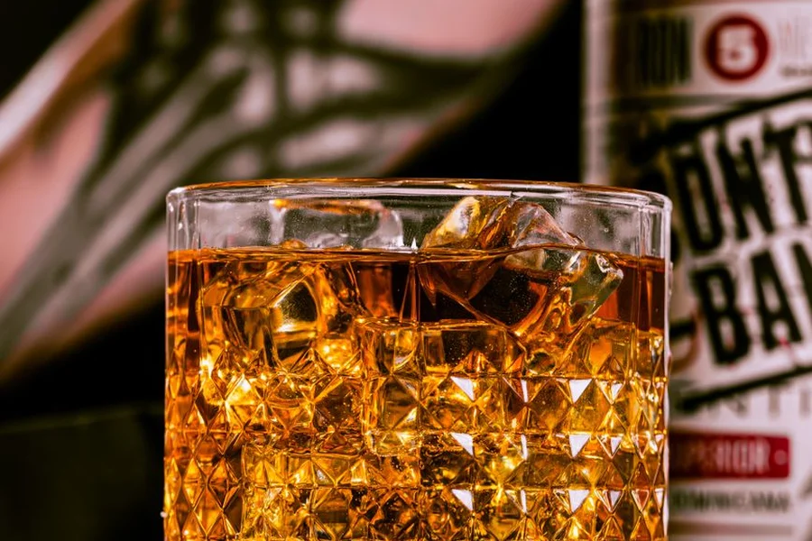 glass of amber bourbon whiskey resting next to oak stave and whiskey bottle