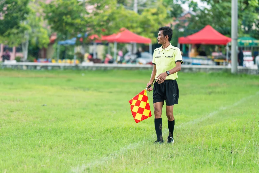 football referee blowing whistle and holding penalty flag on field during game