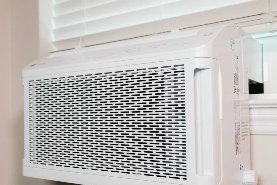 Energy Efficient Window Air Conditioner Cooling Homeowner holding electric utility bill next to residential window air conditioning unit