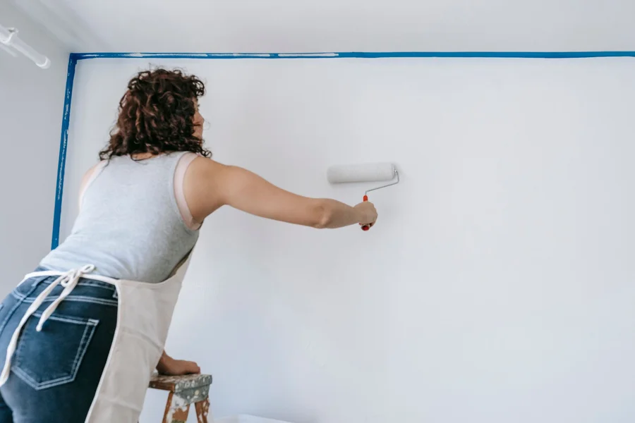 Interior Wall Painting with Roller homeowner using paint roller to apply white paint to living room drywall