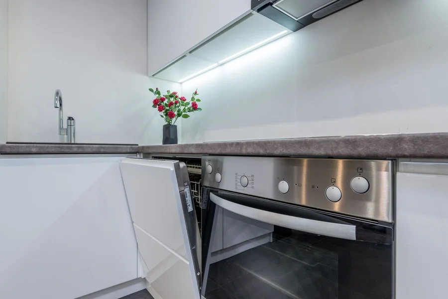 Modern compact stainless steel dishwasher open in bright residential kitchen